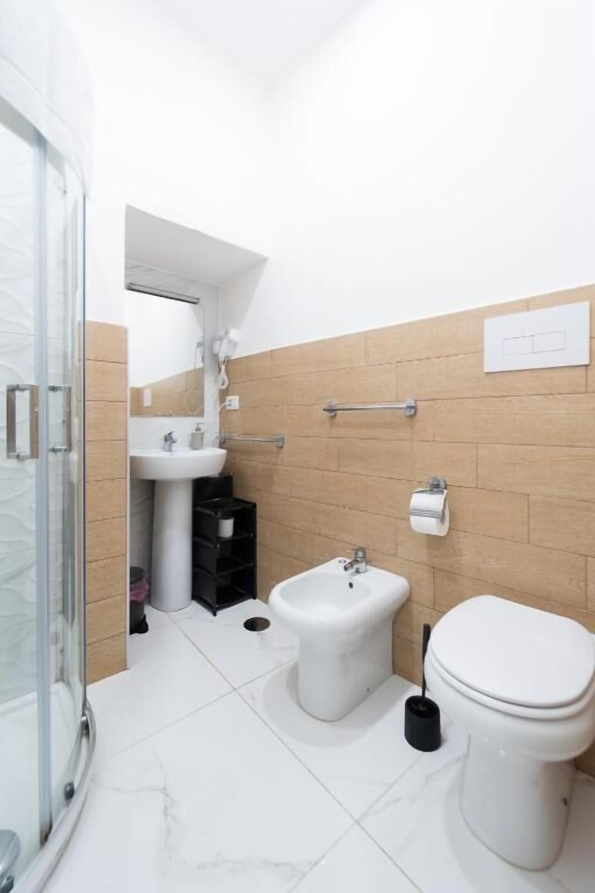 A bathroom with a glass shower enclosure, a pedestal sink, a bidet, and a toilet.
