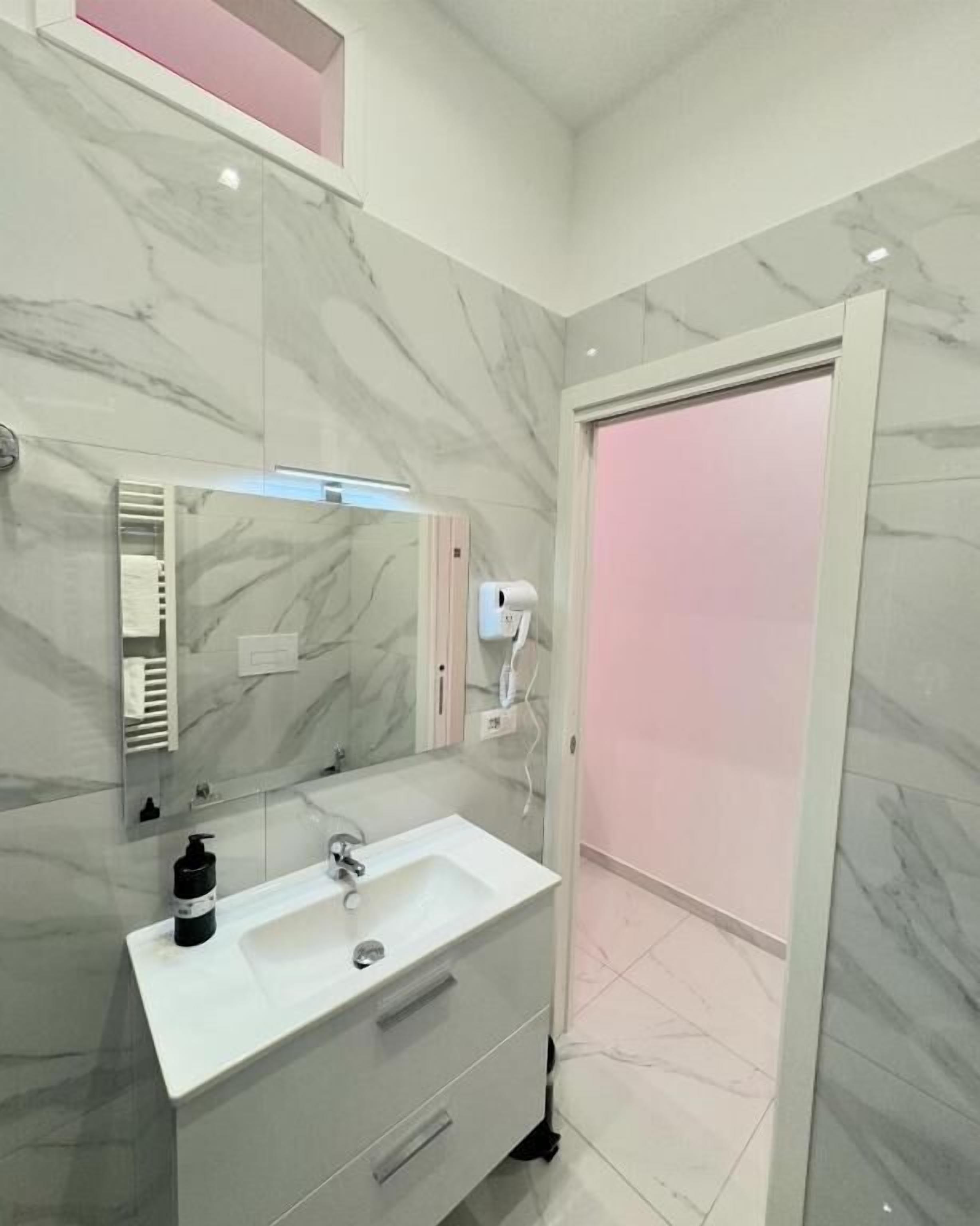 A modern bathroom with a marble vanity, a mirror, a towel dispenser, and a shower area.