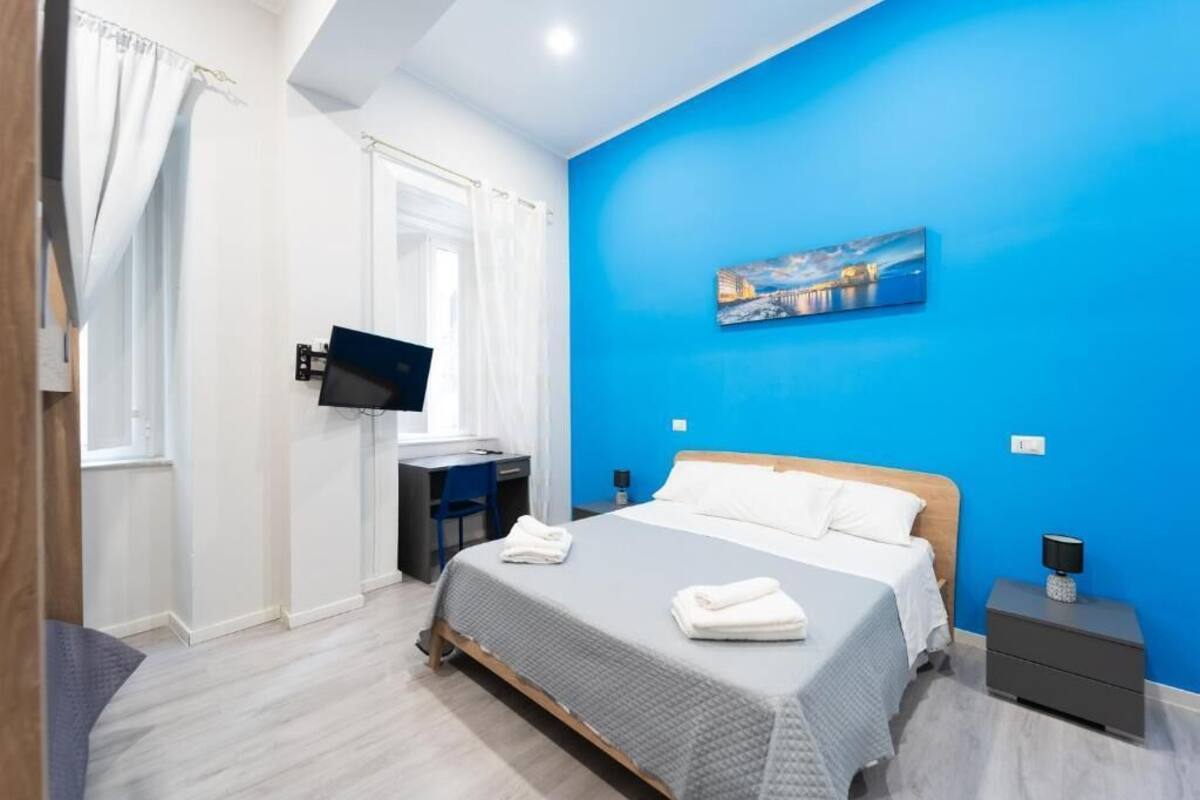 Um quarto com uma cama, uma escrivaninha, uma televisão e um quadro na parede.