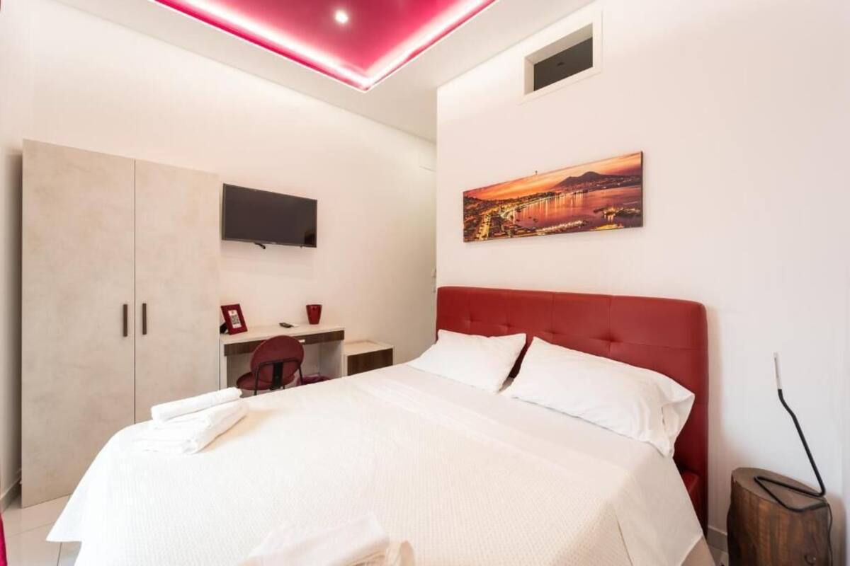Quarto de hotel moderno com cama, escrivaninha, cadeira, TV fixada na parede e um quadro.