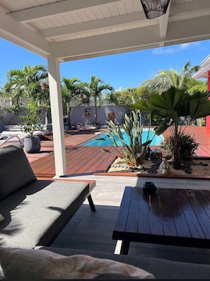 A covered outdoor area with a pool, wooden deck, and seating. - Villa PISCINE JACUZZI. 6 People 3 Bedrooms 3 SD (Saint-François)
