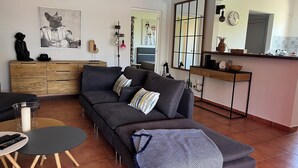 Un salon moderne comprenant un canapé, une table basse, un coin repas avec un comptoir de cuisine et un grand miroir.
