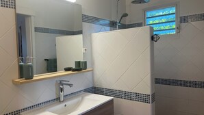 Une salle de bain moderne avec un grand miroir, un lavabo, une douche et une petite fenêtre.