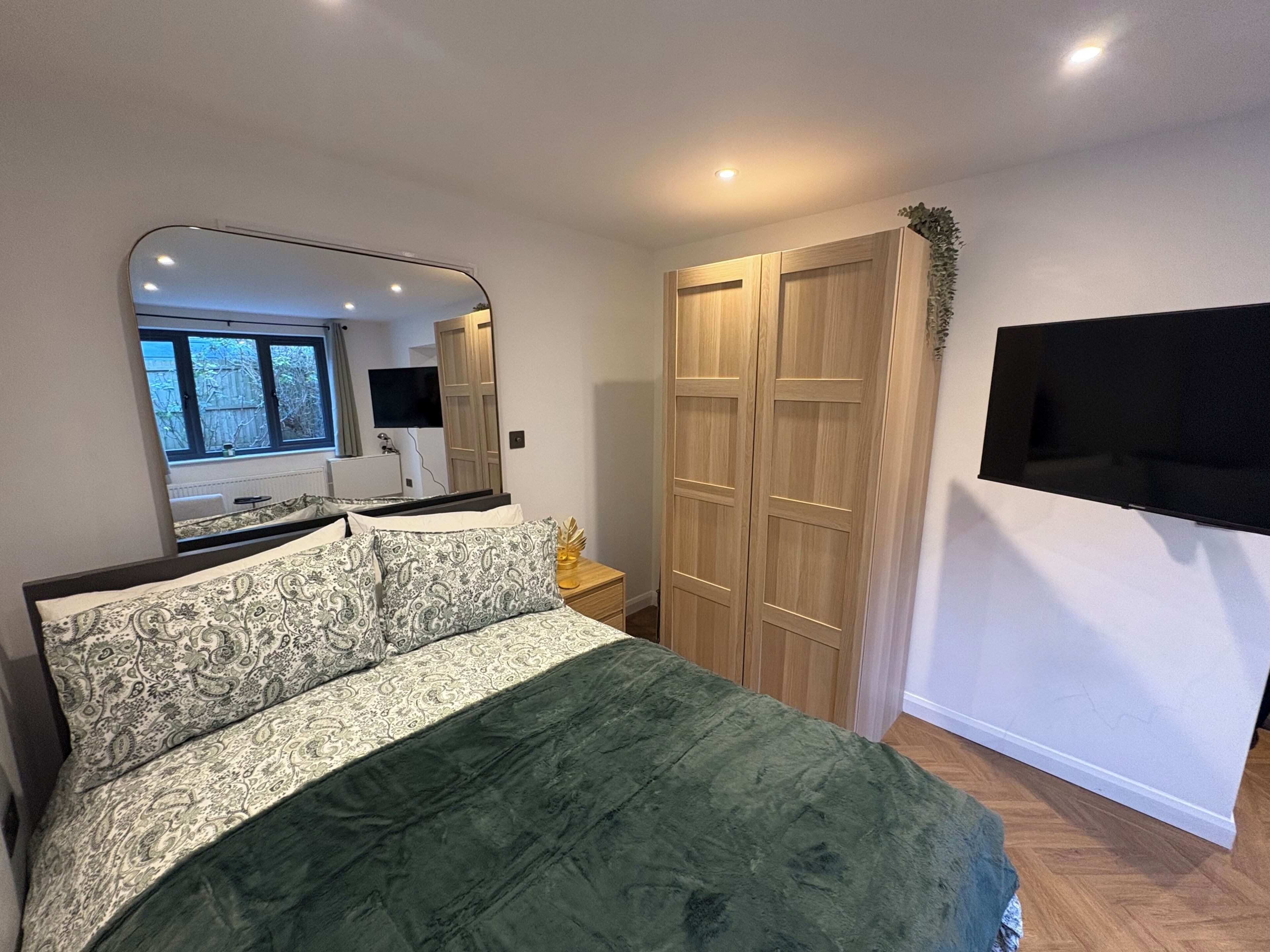 Une chambre à coucher comprenant un lit, un grand miroir, une armoire et un téléviseur fixé au mur.