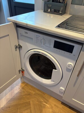 Lavadora de carga frontal con panel de control, un compartimento de almacenamiento pequeño y una puerta con cerradura.