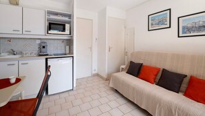 Un espace de vie compact comprenant un coin cuisine, un canapé avec des coussins et deux tableaux encadrés accrochés au mur.