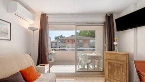 Une chambre d’hôtel comprenant un lit, une petite table, une armoire, une télévision et un balcon avec vue sur les immeubles.