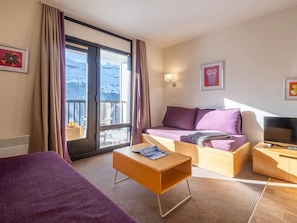Une chambre d’hôtel comprenant un lit, un canapé, une table basse, une télévision et un balcon avec vue sur la montagne.
