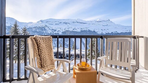 Ein Balkon mit zwei weißen Stühlen, einer gewebten Decke und einem Tablett mit Getränken.