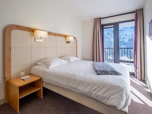 Une chambre d’hôtel avec un lit, une table de chevet et une fenêtre donnant sur un paysage enneigé.