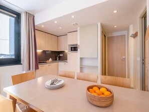 Une cuisine moderne avec un coin repas, un four à micro-ondes et un panier d’oranges sur la table.