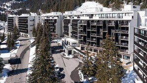 Ein modernes, mehrgeschossiges Hotel mit Innenhof, umgeben von schneebedeckten Bergen und Kiefern.