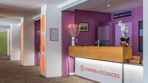 Ein Empfangsschalter mit einem Schild für das Hotel 'Pierre & Vacances', einer violetten Wand und einer Holztresen.