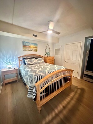 Ein Schlafzimmer mit einem hölzernen Bett, einem Nachttisch, einer Kommode, einem Deckenventilator, einem Bild an der Wand und einer Tür.