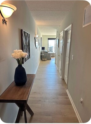 Ein Flur mit Holzboden, einem Tisch mit Blumenvase, Wandleuchten und Blick auf einen Balkon.
