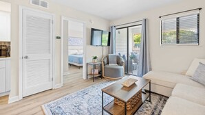 En moderne stue med en sofa, et sofabord, et fjernsyn og en skydedør, der fører ud til en balkon.