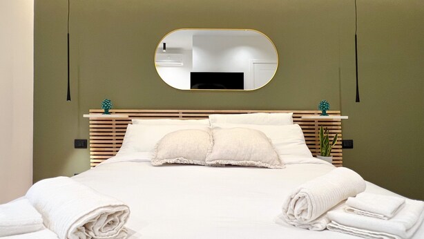 Un lit bien fait, avec du linge de lit et des serviettes blanches, un miroir rond accroché au mur et une tête de lit en bois.