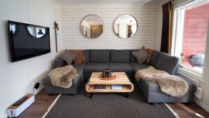Een woonkamer met een hoekbank, een salontafel, een flatscreen televisie en twee spiegels aan de muur.