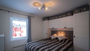 Een slaapkamer met een bed, een raam met gordijnen, een plafondlamp en inbouwmeubels.