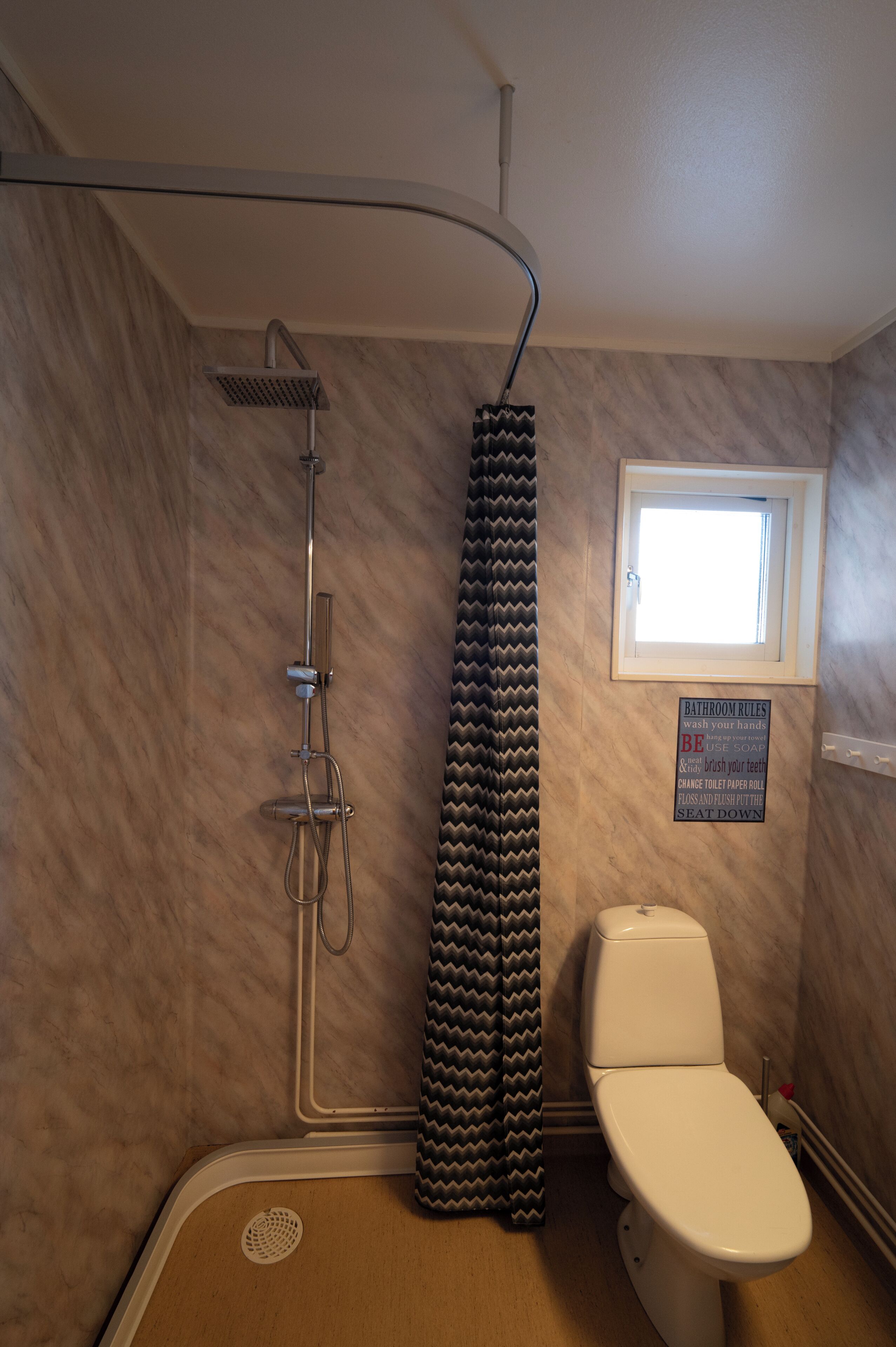 A bathroom with a shower, toilet, and a window.