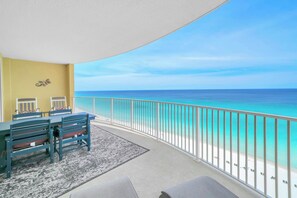A balcony with a view of the beach, a dining table, chairs, and a rug. - ☀️Gulf Front | Free Beach Service | Gorgeous Views | Emerald Isle 1207🌴 (Panama City Beach)