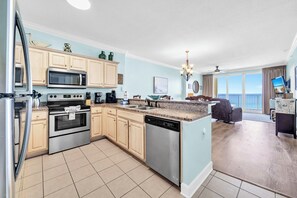 A modern kitchen with a dishwasher, oven, microwave, and a dining area with a view. - ☀️Gulf Front | Free Beach Service | Gorgeous Views | Emerald Isle 1207🌴 (Panama City Beach)