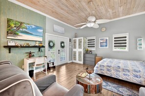 A bedroom with a bed, a desk, a chair, a ceiling fan, and a large window. - Adorable Estero Cottage - Heated Pool/Spa - Sauna (Estero)
