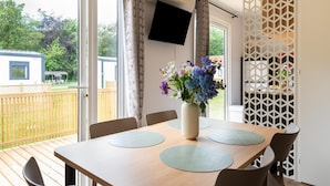 Ein Essbereich mit Tisch, Stühlen, einer Blumenvase, einem Fernseher und Blick ins Freie.