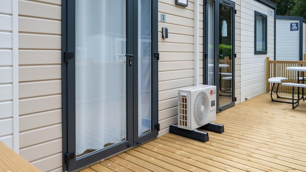 Ein eingeschossiges Mobilheim mit einer Terrasse, einer Schiebetür und einer Klimaanlage.