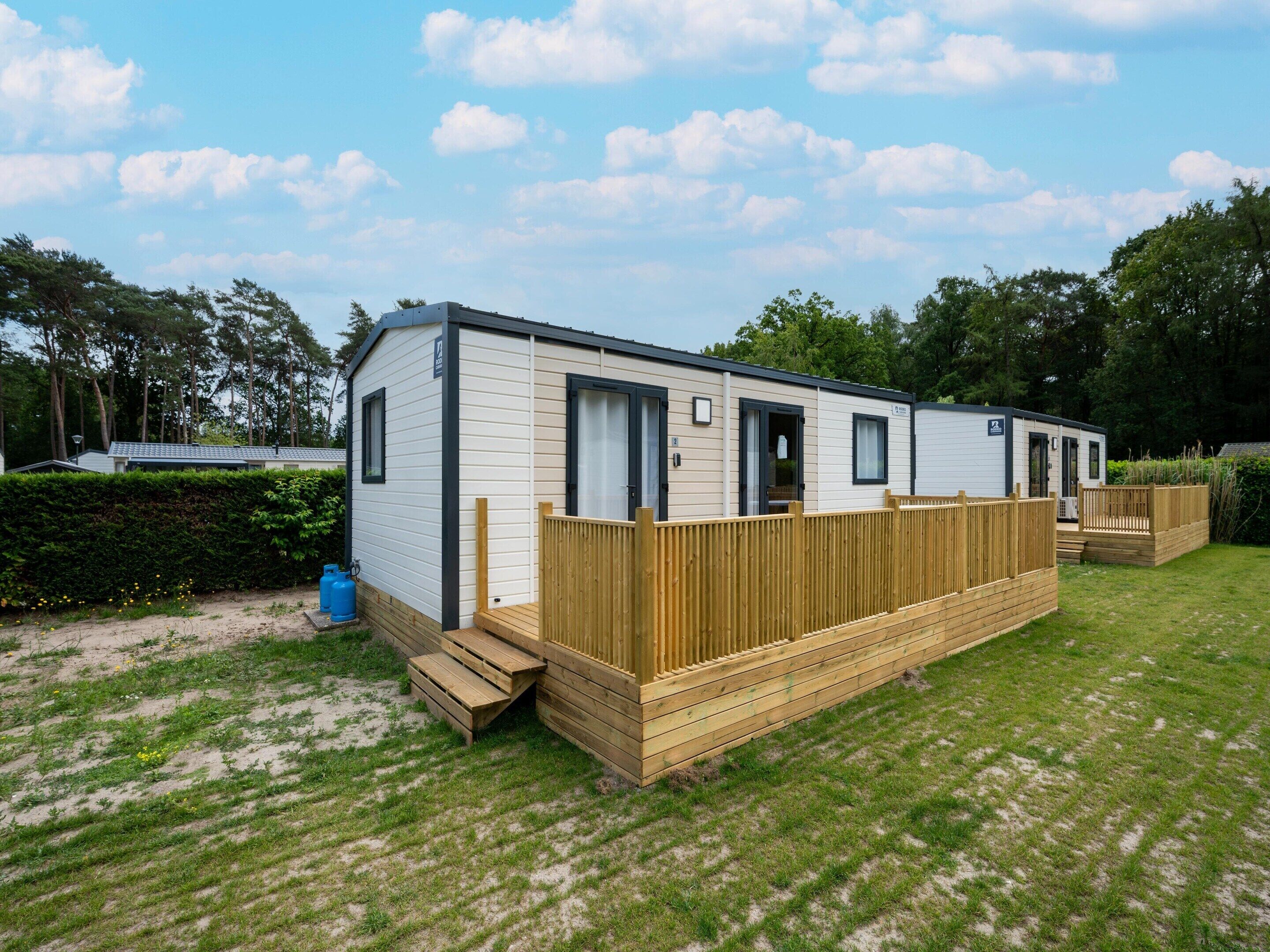 A mobile home with a wooden deck, a small porch, and a fenced yard.