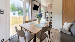 Ein modernes Zimmer mit einem Holzespeisetisch, Stühlen, einer Couch, einem Fernseher und Blick auf eine Holzterrasse.