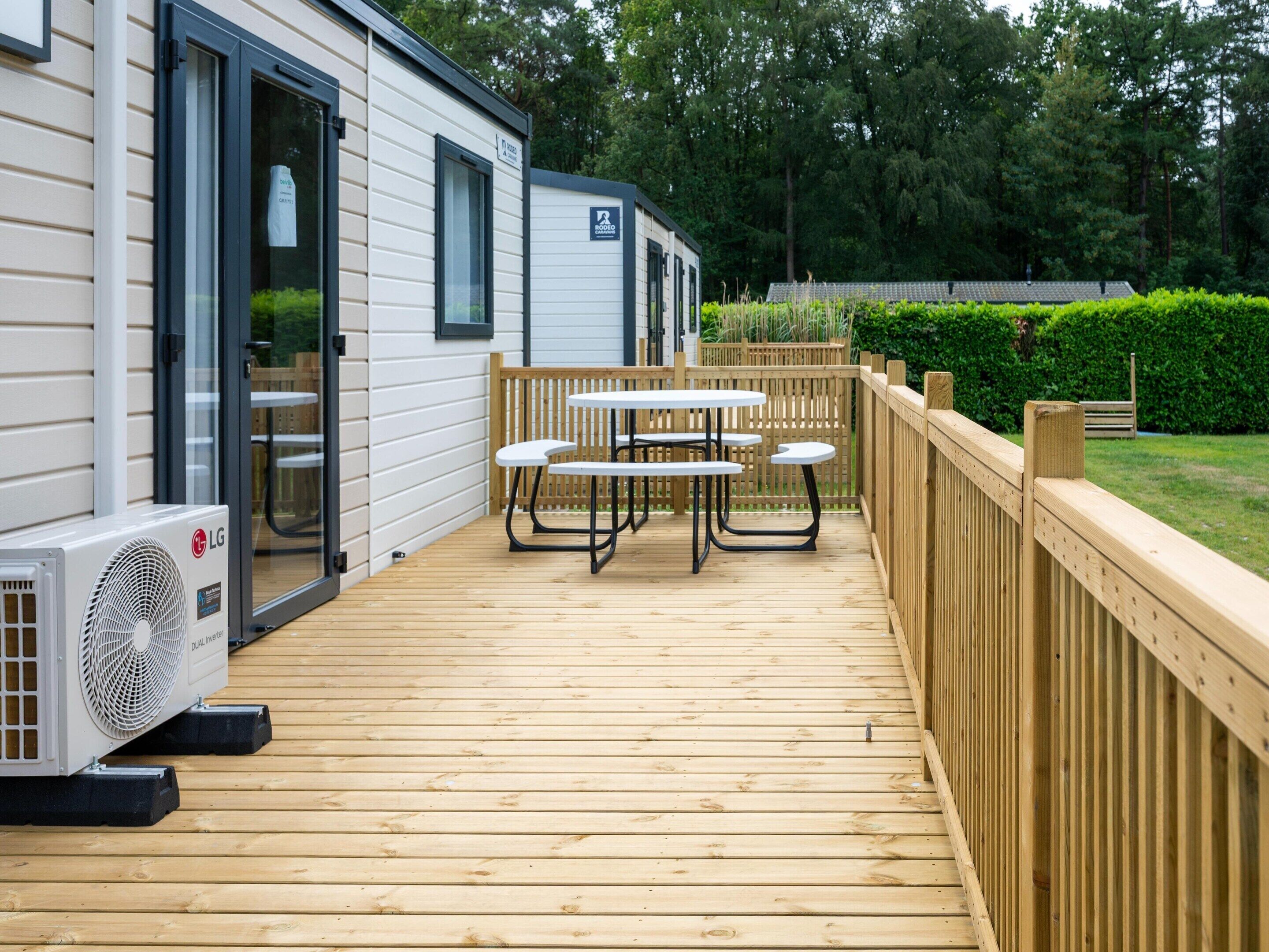 A wooden deck with picnic tables, an air conditioning unit, and a wooden fence.