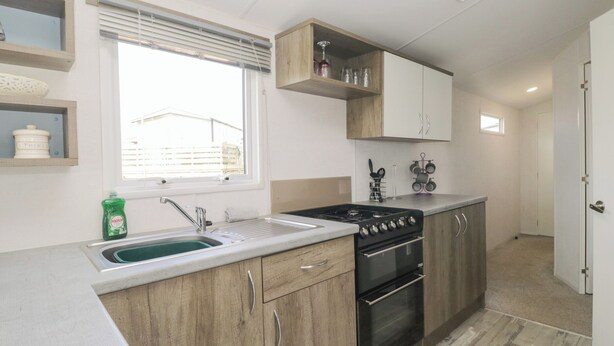 A compact kitchen with a sink, stove, oven, and wooden cabinets. - Standard Caravan at Three Lochs Holiday Park (Newton Stewart)