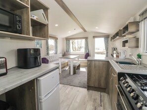 Une cuisine compacte équipée d’un réfrigérateur, d’un four à micro-ondes, d’un grille-pain et d’une cuisinière. On y trouve également un coin repas avec une table et des chaises, ainsi qu’une fenêtre avec des rideaux.