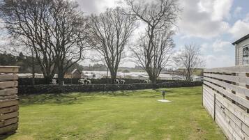 A grassy outdoor area with a stone wall, trees, and a building in the background.