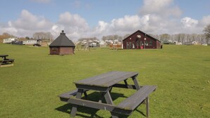 A picnic table in a grassy field with a red building in the background. - Standard Caravan at Three Lochs Holiday Park (Newton Stewart)