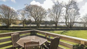 A wooden deck with a table and chairs, overlooking a grassy area with trees and distant buildings.