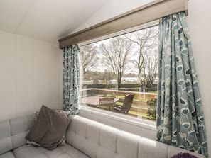 A room with a large window, a sofa, and a view of the outdoors. - Standard Caravan at Three Lochs Holiday Park (Newton Stewart)