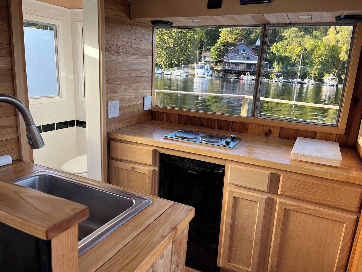 Une cuisine de taille réduite avec une fenêtre donnant sur un lac et des bateaux amarrés.