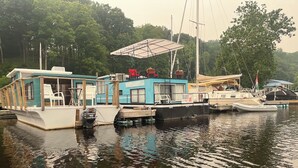 En flydende konstruktion med et overdækket siddeområde, en lille båd ligger til anker i nærheden, og et flag vaje.