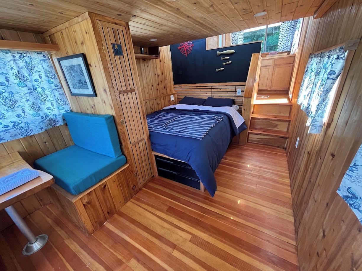 Quarto compacto com cama, um banco estofado azul e uma mesa pequena.