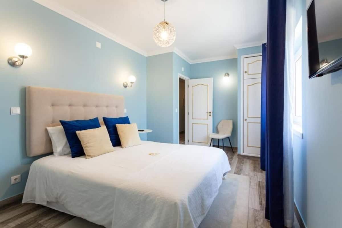 A bedroom with a large bed, a bedside table, a chair, a TV, and a door.