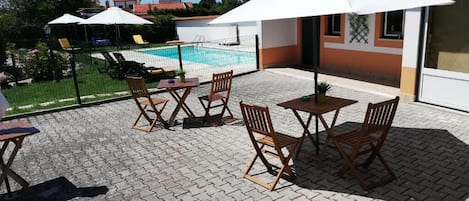 A patio with outdoor seating, a swimming pool, and a building with a tiled roof.