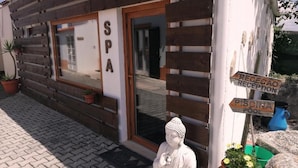 Ein Spa-Gebäude mit Holzfassade, einer sitzenden Buddha-Statue und einem Schild, das Rezeption und Pool anzeigt.