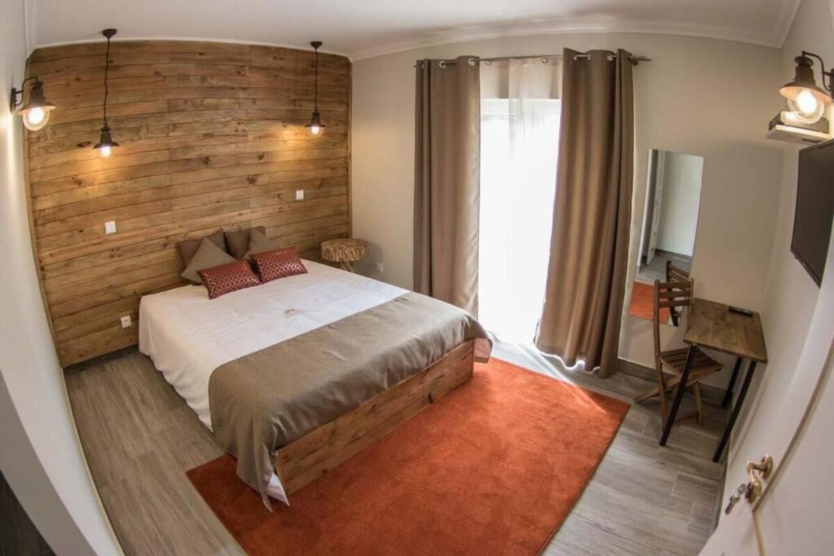A bedroom with a wooden headboard, a bed with a red pillow, a desk with a chair, and a mirror.