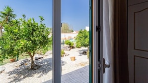 Blick durch eine Glastür auf einen Garten mit einem kleinen Baum, Kiesweg und Kübelpflanzen.