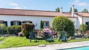 Ein Pool mit geschwungener Kante, umgeben von einer Terrasse mit Stühlen und einem kleinen Garten mit verschiedenen Pflanzen und Blumen.