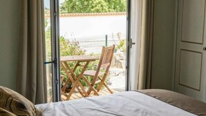 Ein Schlafzimmer mit Bett, Fenster und Blick auf eine Terrasse mit Tisch und Stühlen.