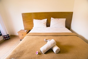 A hotel room with a bed, pillows, a wooden headboard, a nightstand, and a brown carpet. - Villa Karang Homestay (Gili Air)