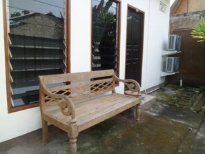A wooden bench outside a building with a window and door, and an air conditioning unit on a shelf.